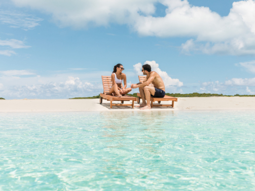 imagem mostra um casal de pessoas brancas à beira do mar em out Islands, nas Bahamas.